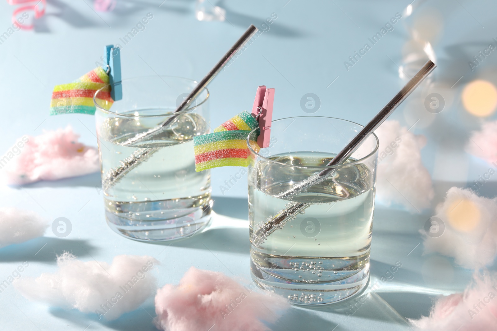 Photo of Tasty cocktails in glasses decorated with gummy candies and cotton candy on light blue background