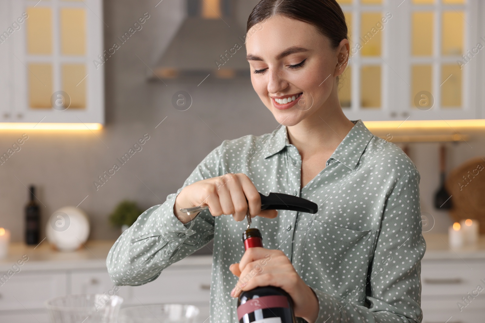 Photo of Woman opening wine bottle with corkscrew in kitchen