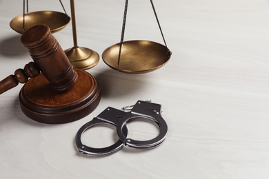 Judge's gavel, handcuffs and scales on white wooden background. Criminal law concept