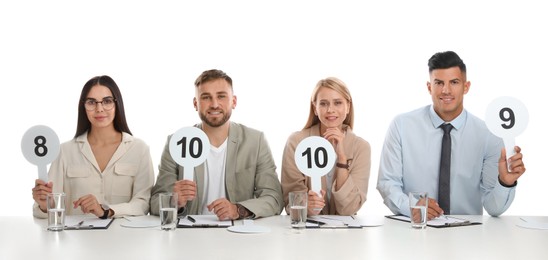 Panel of judges holding different score signs at table on white background