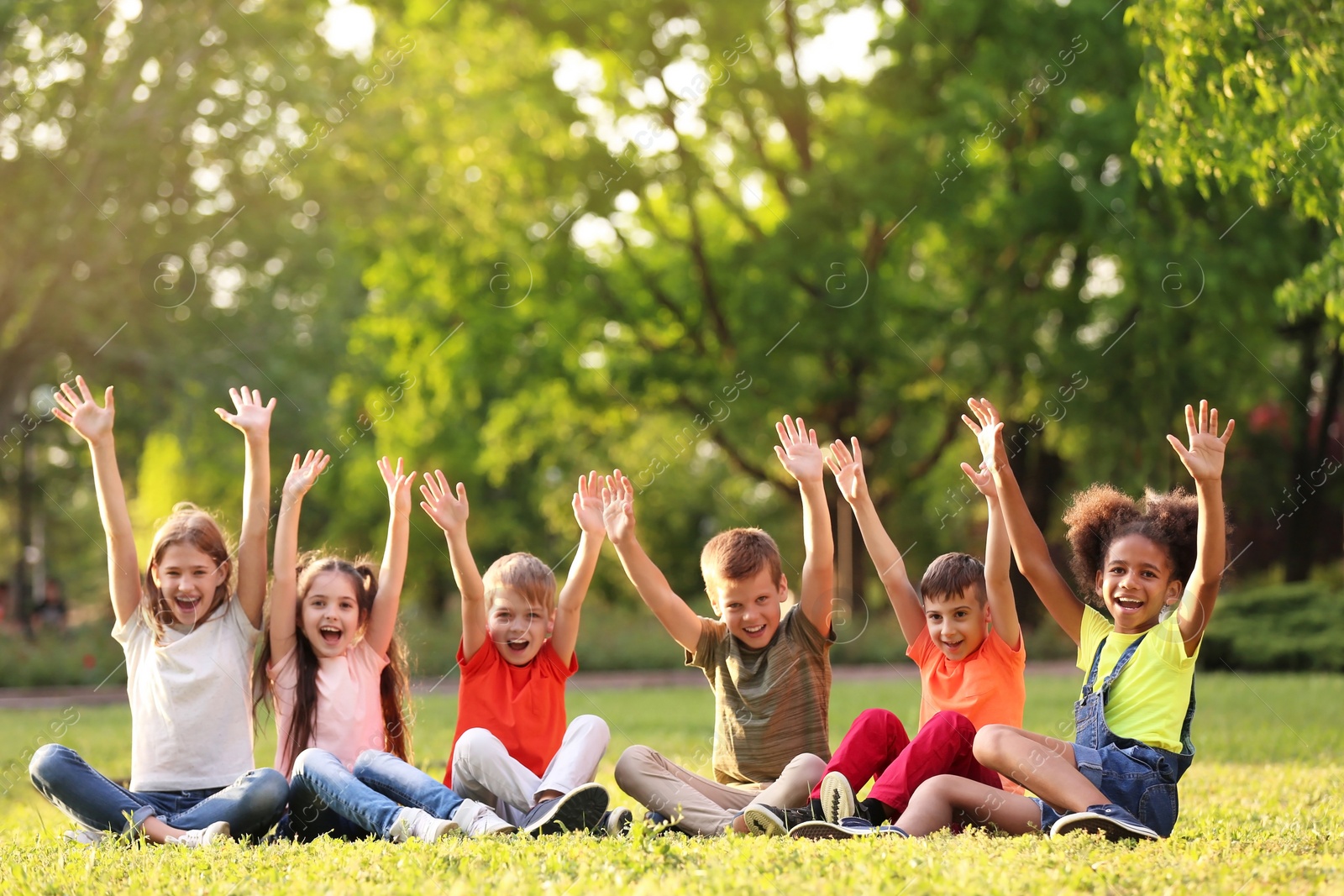 Photo of Cute little children sitting on grass outdoors on sunny day