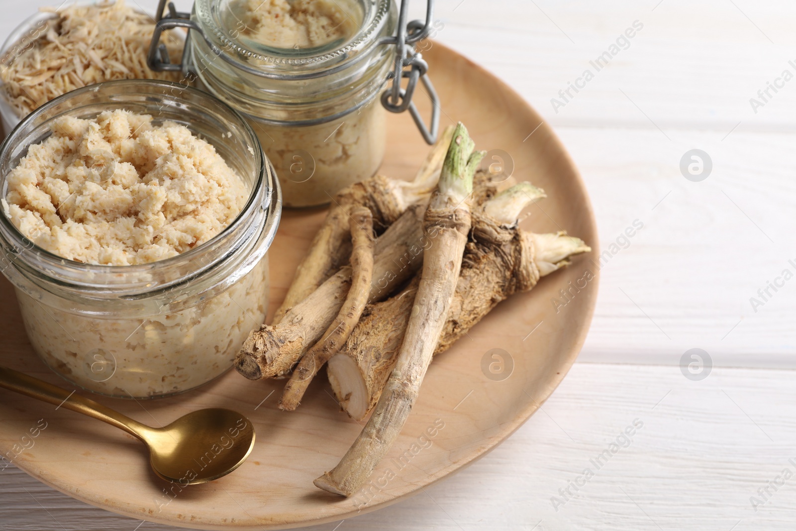 Photo of Platter with tasty prepared horseradish and roots on white wooden table, closeup
