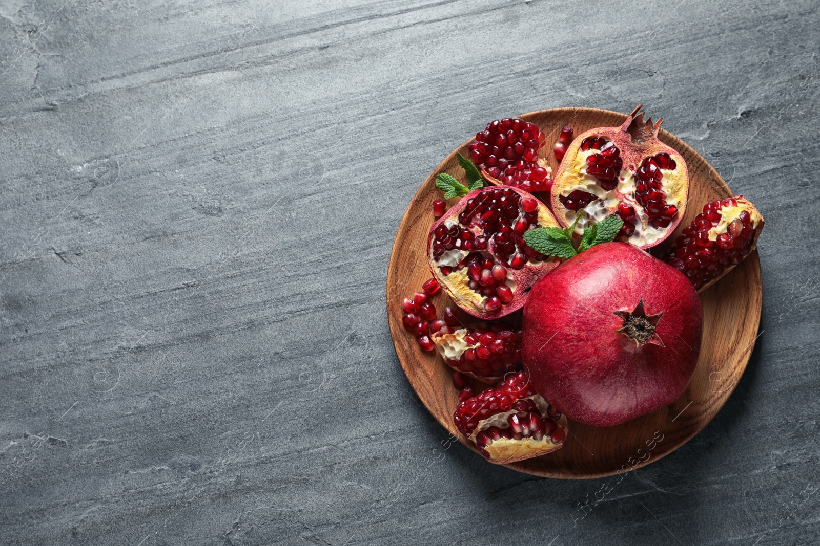 Photo of Plate of ripe pomegranates on grey background, top view with space for text