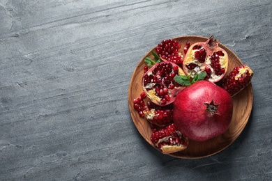 Photo of Plate of ripe pomegranates on grey background, top view with space for text