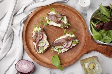 Delicious bruschettas with anchovies, cream cheese, red onion and greens on white marble table, flat lay