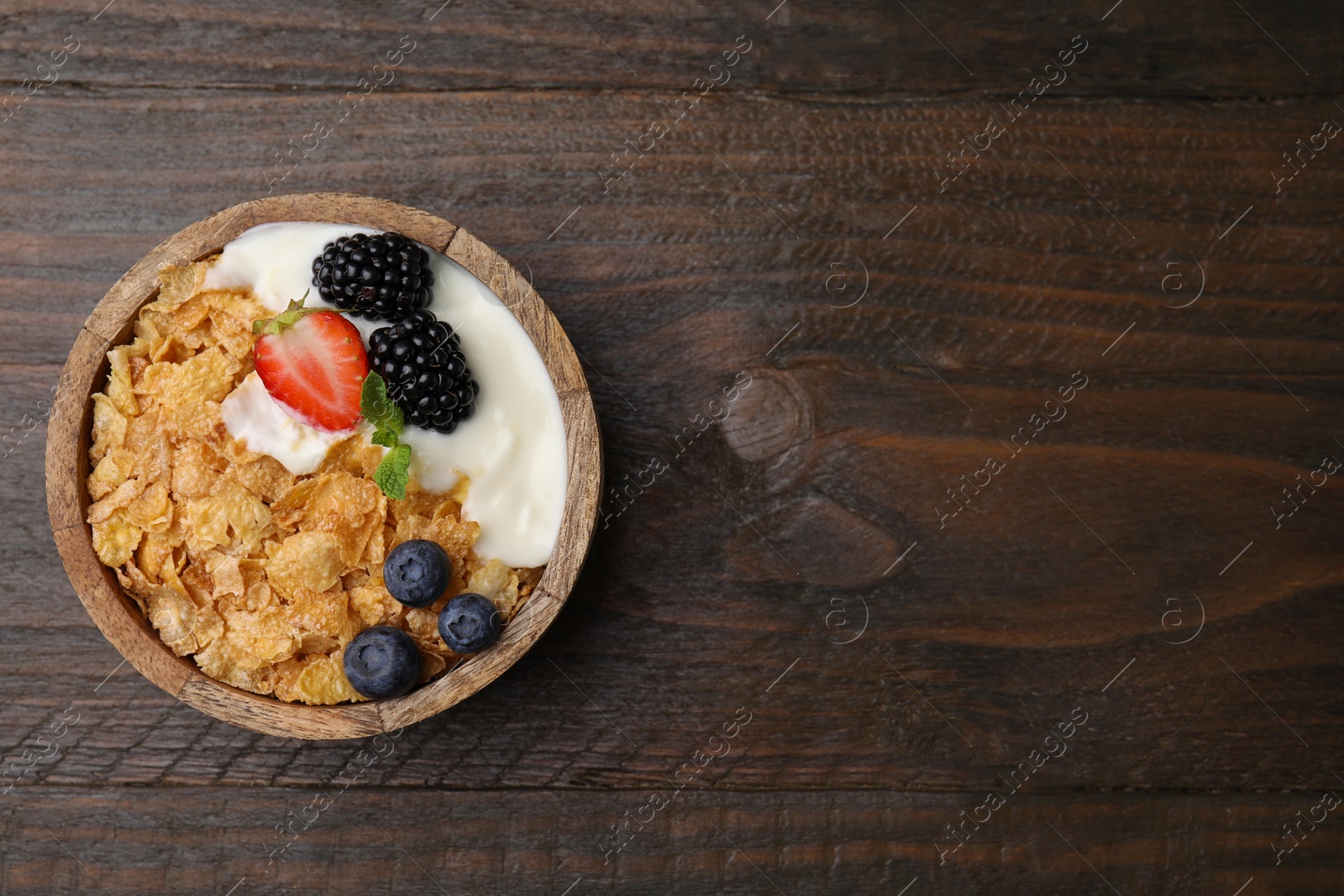 Photo of Delicious crispy cornflakes, yogurt and fresh berries in bowl on wooden table, top view with space for text. Healthy breakfast