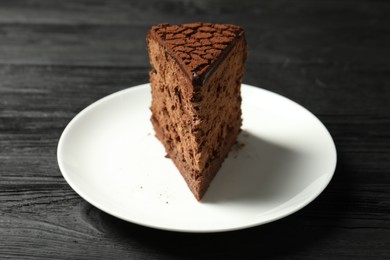 Photo of Piece of delicious chocolate truffle cake on black wooden table, closeup