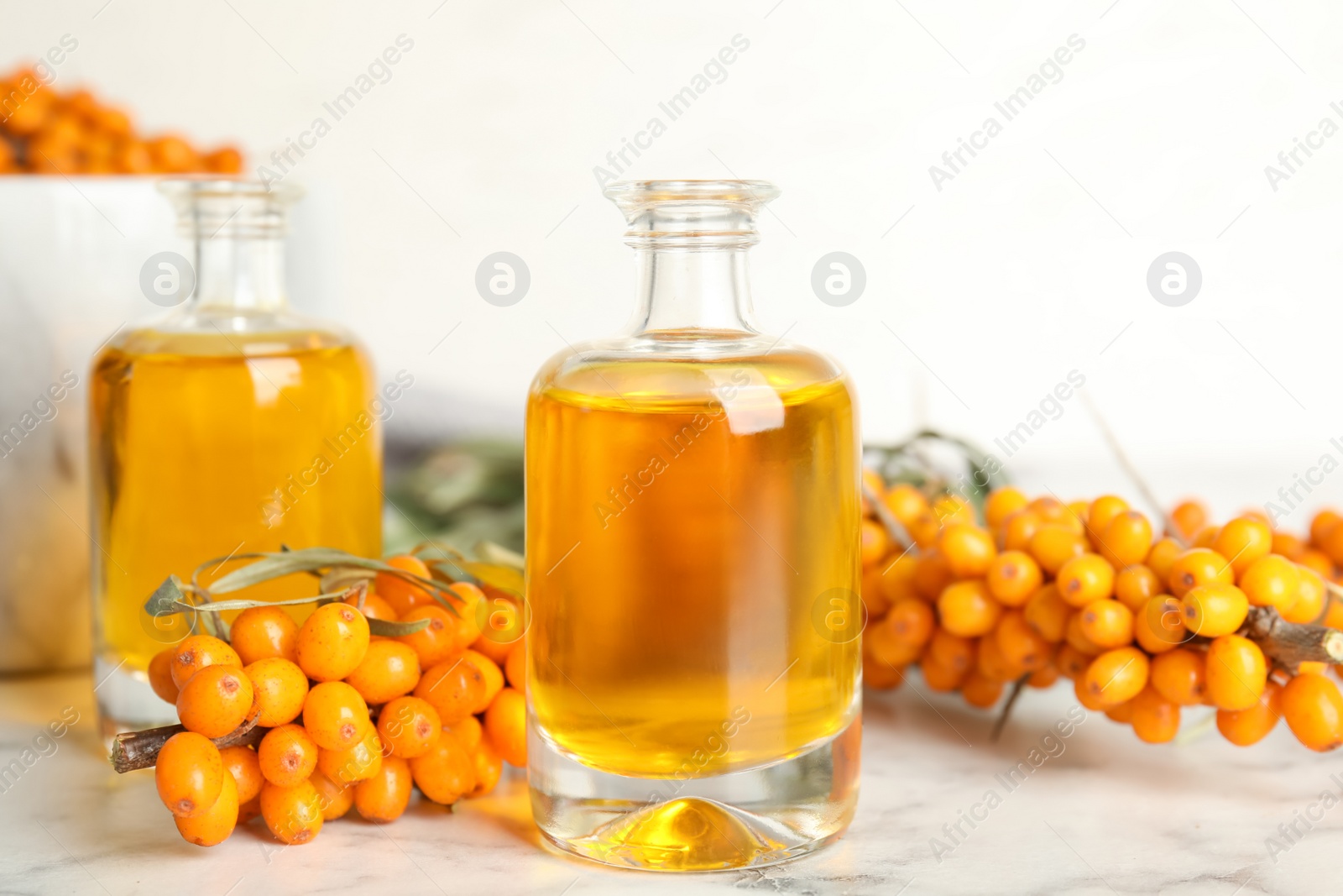 Photo of Natural sea buckthorn oil and fresh berries on white marble table