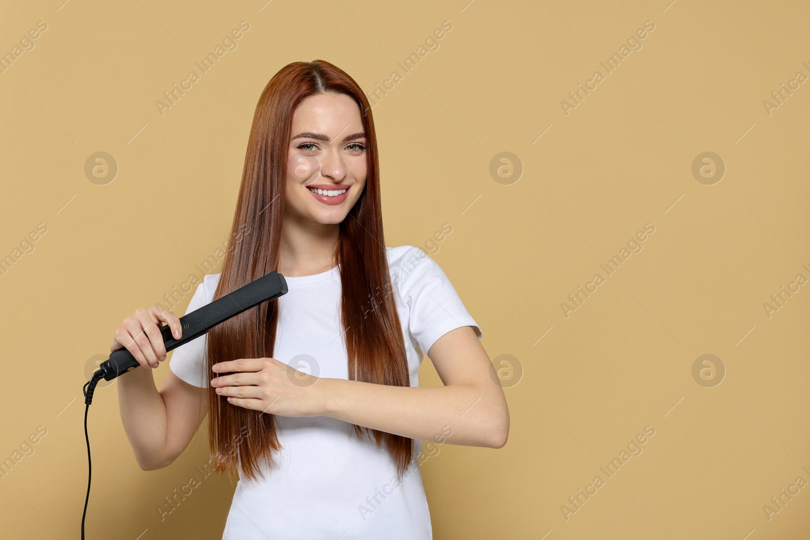 Photo of Beautiful woman using hair iron on beige background, space for text