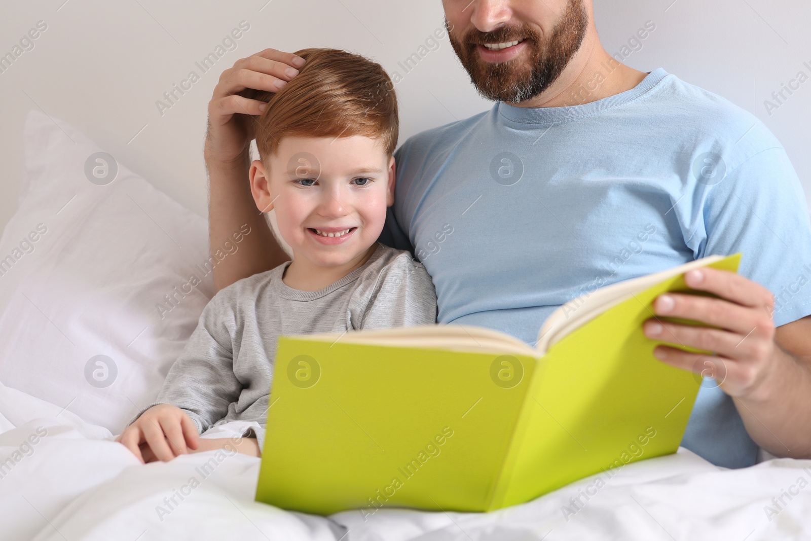 Photo of Father reading book with his child on bed at home