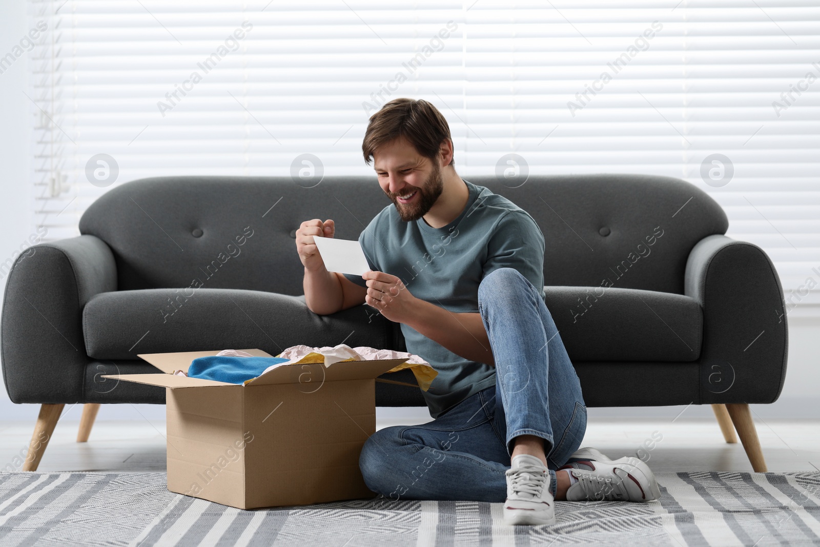 Photo of Happy man with greeting card near parcel at home. Internet shopping