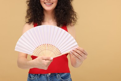 Woman holding hand fan on beige background, closeup. Space for text