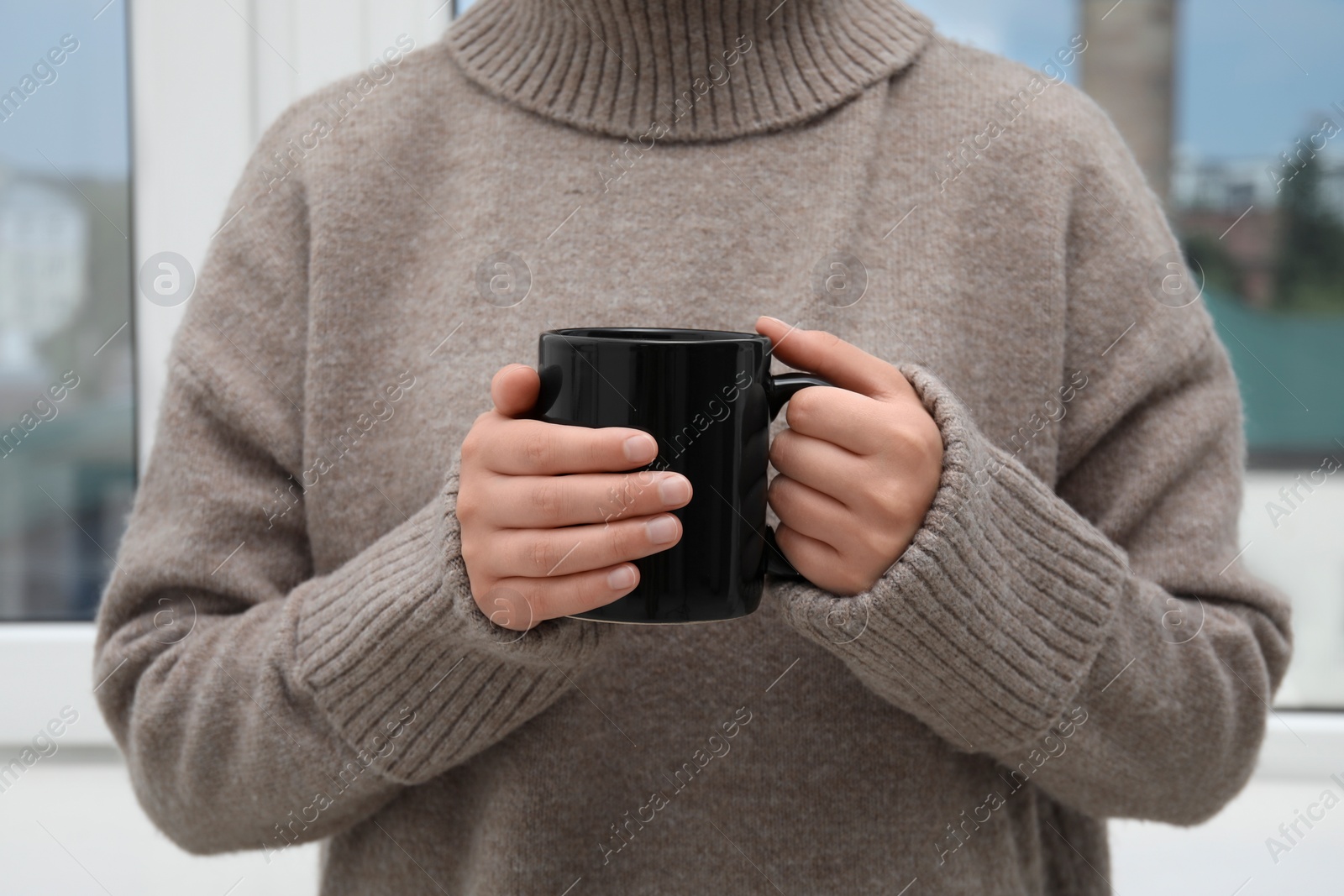 Photo of Woman holding black mug indoors, closeup view