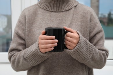 Photo of Woman holding black mug indoors, closeup view