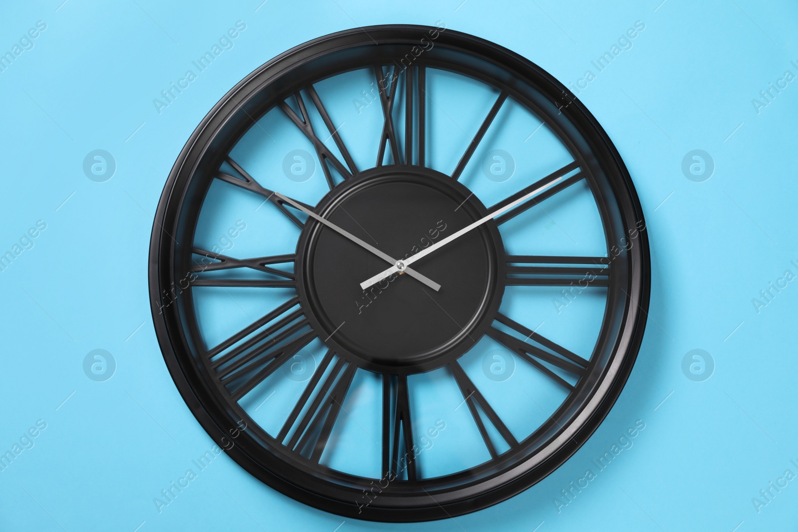 Photo of Stylish analog clock hanging on light blue wall