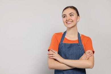 Photo of Beautiful young woman in clean denim apron on light grey background. Space for text