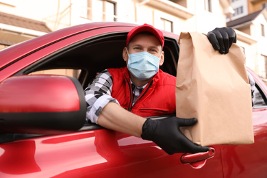 Photo of Courier in protective mask and gloves giving order out of car window outdoors. Food delivery service during coronavirus quarantine
