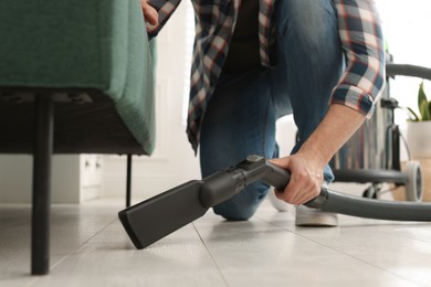 Photo of Man vacuuming floor under sofa in living room, closeup