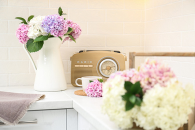 Beautiful hydrangea flowers, cup and radio set on light countertop