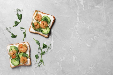 Photo of Tasty toasts with cream cheese, shrimps, cucumbers and microgreens on grey marble table, flat lay. Space for text