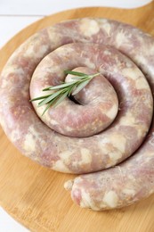 Photo of Raw homemade sausage and rosemary on wooden board, closeup