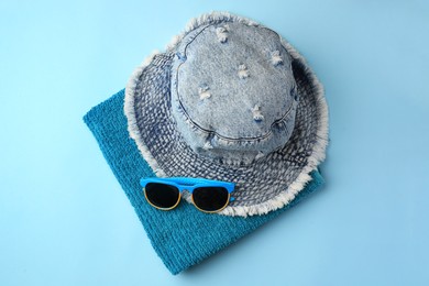 Photo of Towel, denim hat and sunglasses on light blue background, flat lay. Beach accessories