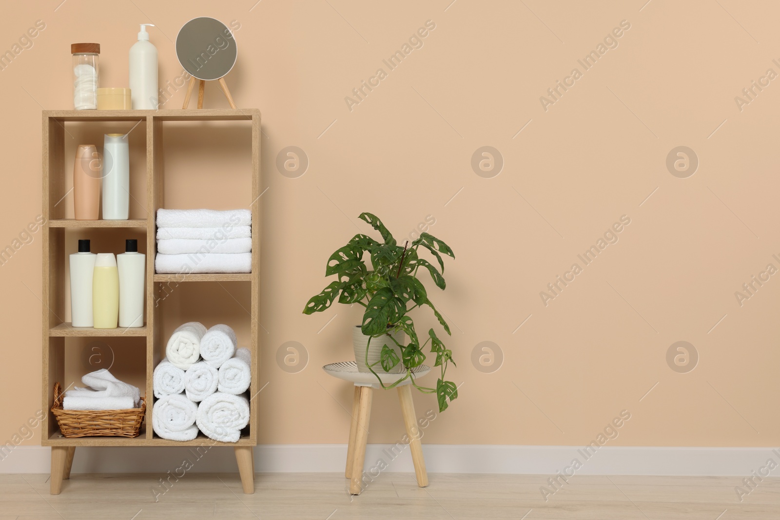 Photo of Soft folded towels and cosmetic bottles on wooden shelving unit near beige wall, space for text
