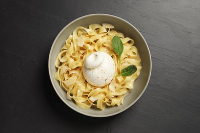 Photo of Delicious pasta with burrata cheese and basil on black table, top view