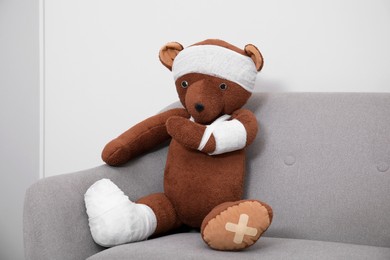 Toy bear with bandages sitting on sofa near light wall