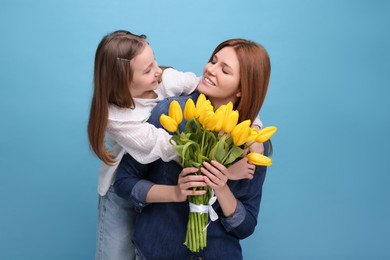 Mother and her cute daughter with bouquet of yellow tulips on light blue background