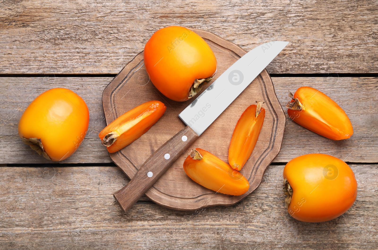 Photo of Delicious ripe persimmons and knife on wooden table, flat lay