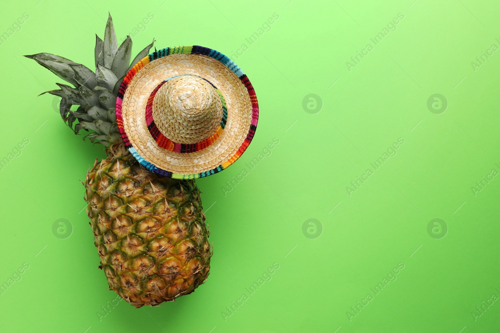 Photo of Mexican sombrero hat and pineapple on green background, top view. Space for text