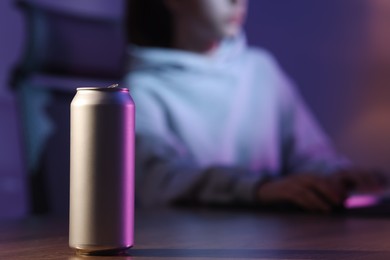 Photo of Girl playing computer game at home, focus on can with energy drink
