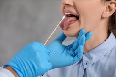 Doctor taking throat swab sample from woman`s oral cavity on blurred background, closeup