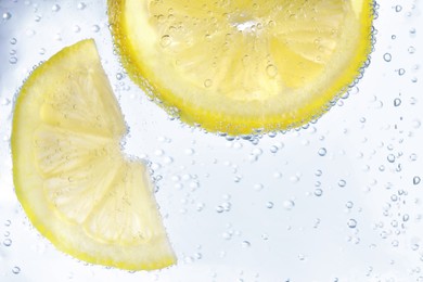 Photo of Juicy lemon slices in soda water, closeup