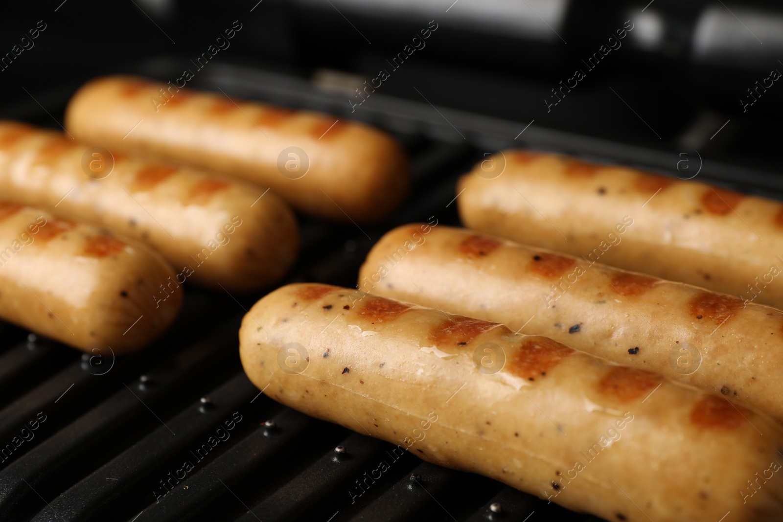 Photo of Delicious vegan sausages cooking on electric grill, closeup