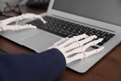 Photo of Human skeleton in suit using laptop at table, closeup