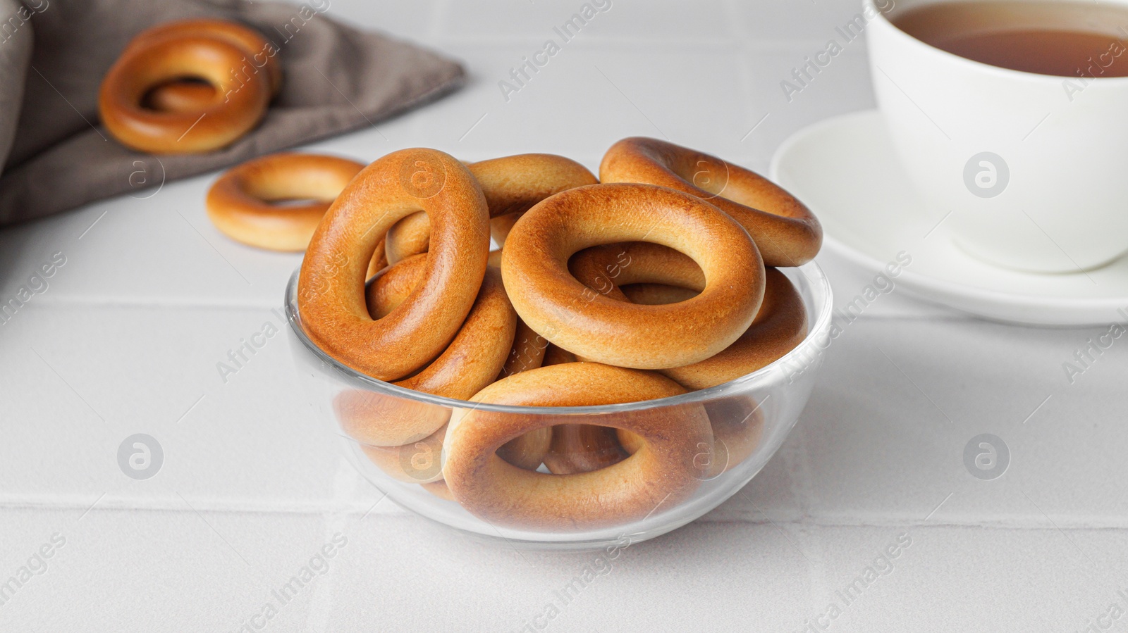 Photo of Bowl with tasty dry bagels (sushki) on white tiled table