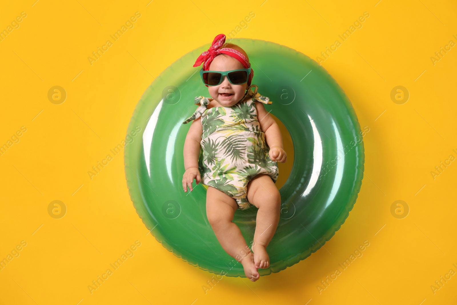 Photo of Cute little baby in sunglasses with inflatable ring on yellow background