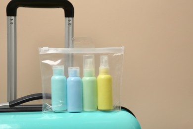 Cosmetic travel kit in plastic bag on suitcase against beige wall, space for text. Bath accessories