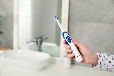 Photo of Woman holding electric toothbrush in bathroom at home, closeup