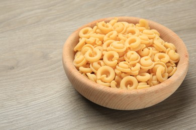 Photo of Raw dischi volanti pasta in bowl on light grey wooden table, closeup. Space for text