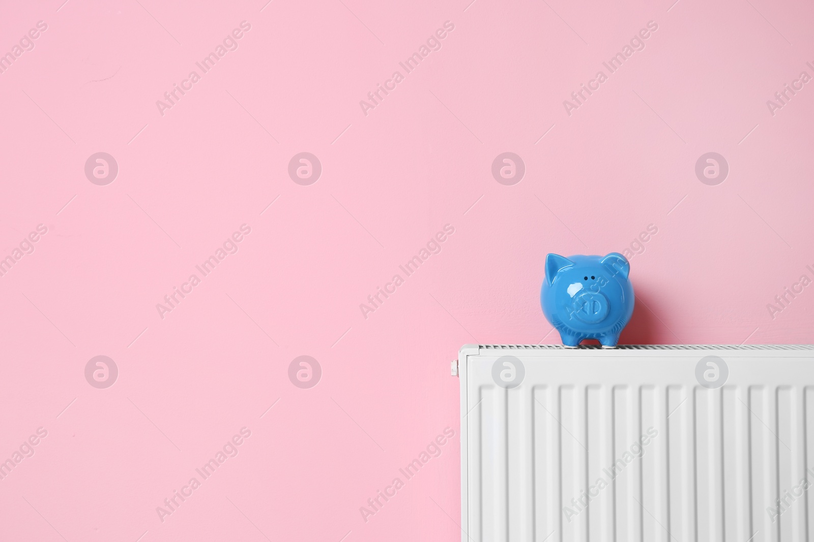 Photo of Heating radiator with piggy bank near color wall. Space for text