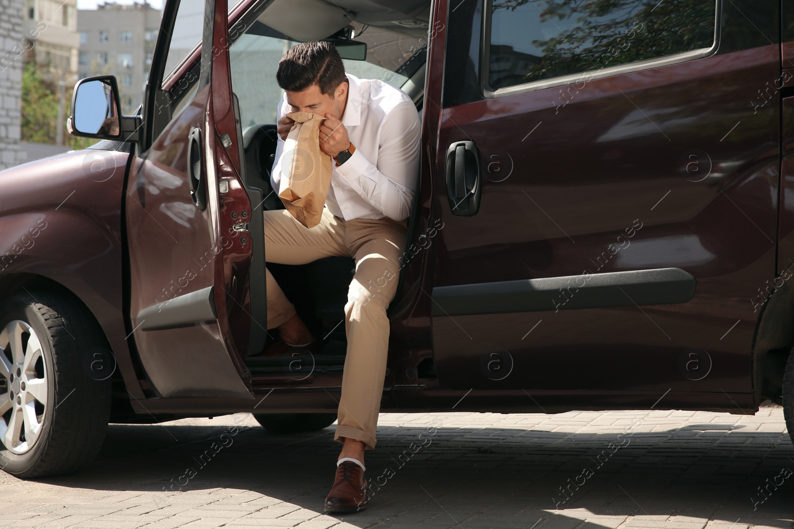 Photo of Man with paper bag suffering from nausea in car