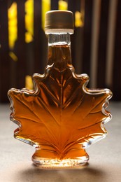 Leaf shaped bottle of tasty maple syrup on light grey table