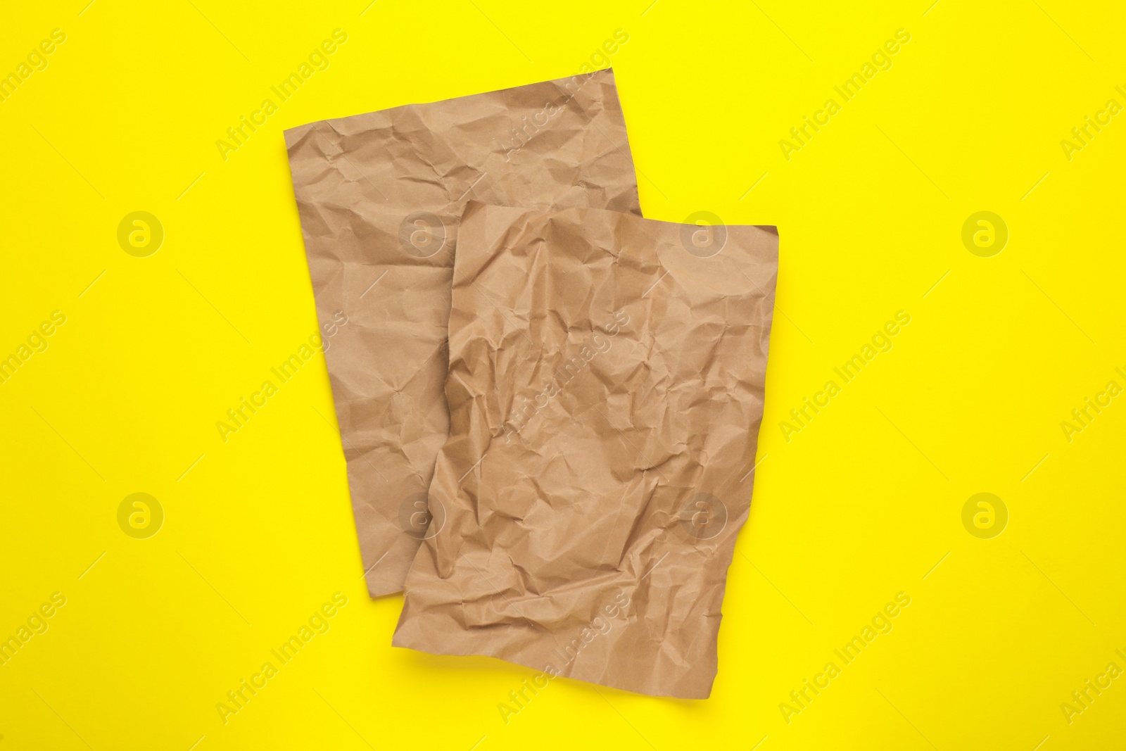 Photo of Sheets of crumpled brown paper on yellow background, top view
