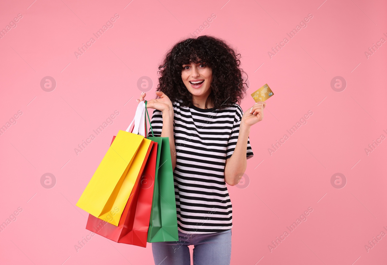 Photo of Happy young woman with shopping bags and credit card on pink background