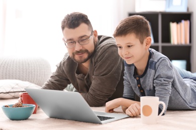 Photo of Little boy and his dad using laptop at home