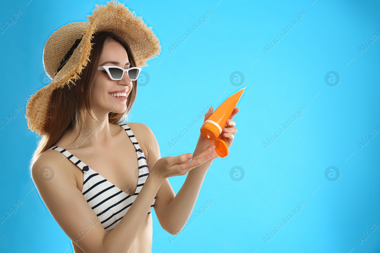 Photo of Young woman applying sun protection cream on light blue background. Space for text