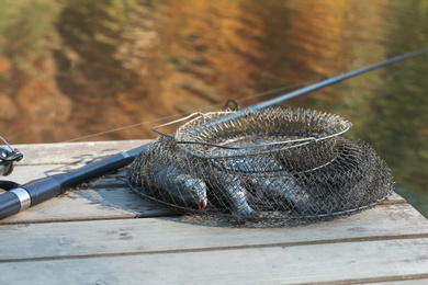 Photo of Fishing rod and fresh fish on wooden pier near pond